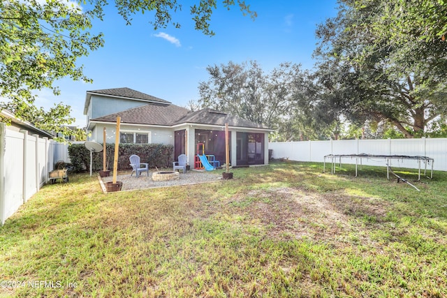 back of house with a trampoline, a sunroom, a fire pit, and a lawn