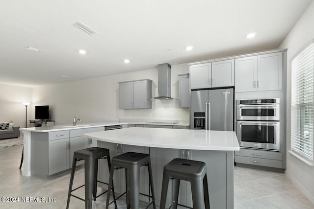 kitchen with gray cabinetry, wall chimney exhaust hood, stainless steel appliances, and a kitchen island