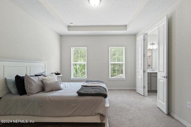 carpeted bedroom featuring a raised ceiling and ensuite bathroom