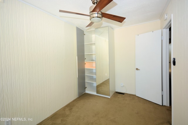 unfurnished bedroom with a closet, a textured ceiling, crown molding, ceiling fan, and light colored carpet