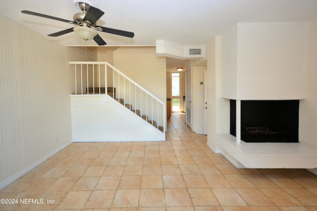 stairway featuring a brick fireplace and ceiling fan