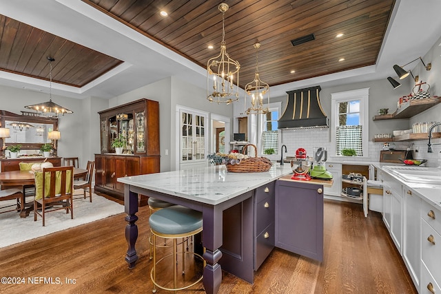 kitchen featuring a kitchen island with sink, pendant lighting, wooden ceiling, dark hardwood / wood-style flooring, and a raised ceiling