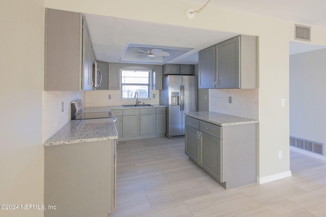 kitchen featuring gray cabinetry, stainless steel appliances, backsplash, sink, and ceiling fan