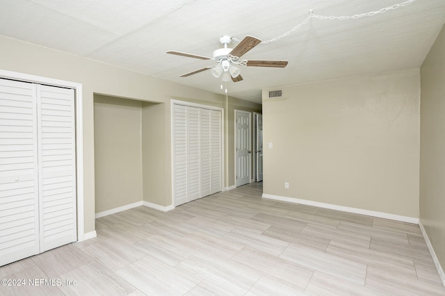 unfurnished bedroom with a textured ceiling, multiple closets, and ceiling fan