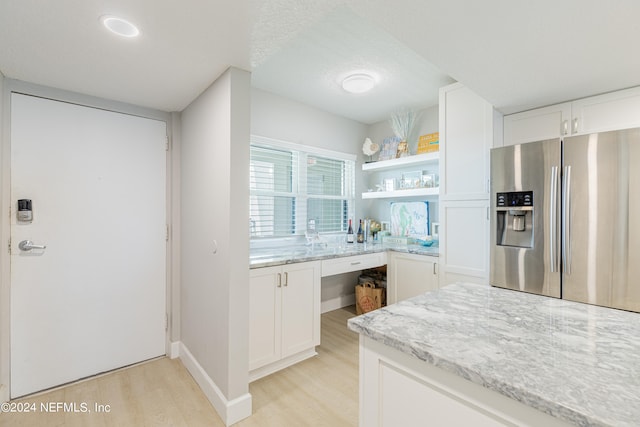 kitchen with light stone counters, stainless steel refrigerator with ice dispenser, light hardwood / wood-style floors, and white cabinetry