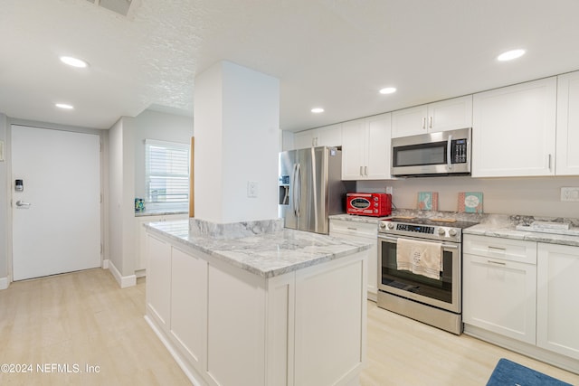 kitchen with light stone counters, appliances with stainless steel finishes, a center island, and white cabinetry