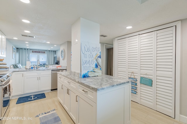 kitchen with a kitchen island, a textured ceiling, white cabinetry, appliances with stainless steel finishes, and light wood-type flooring