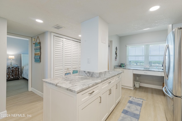 kitchen with white cabinetry, light hardwood / wood-style floors, light stone counters, and stainless steel refrigerator