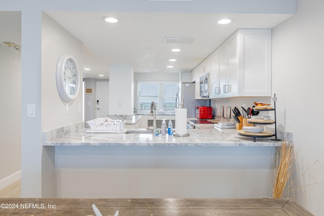 kitchen with light stone counters, white cabinets, sink, kitchen peninsula, and appliances with stainless steel finishes