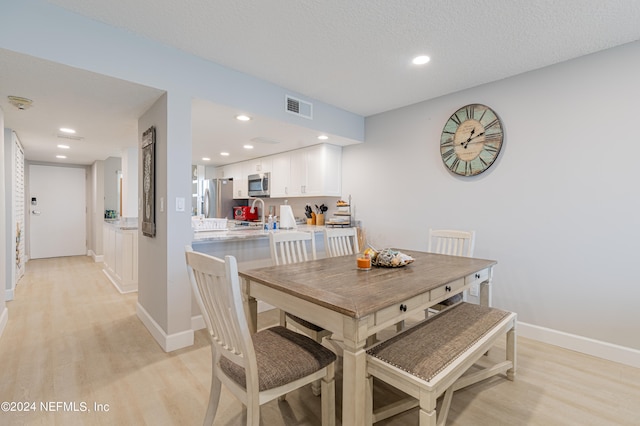 dining space featuring light wood-type flooring and a textured ceiling