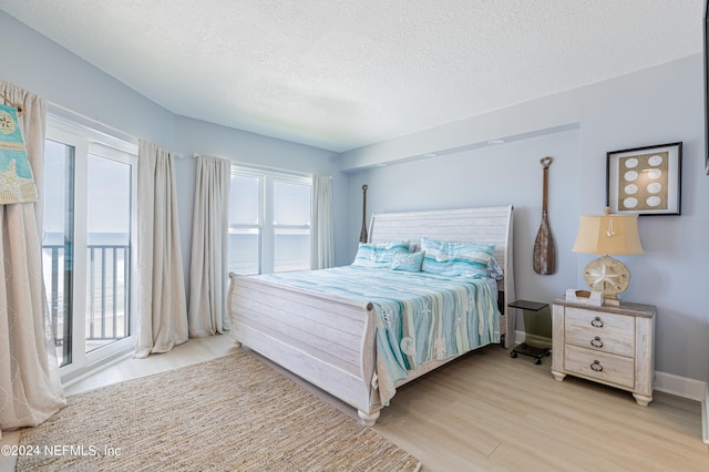 bedroom featuring access to exterior, a textured ceiling, light hardwood / wood-style floors, and a water view