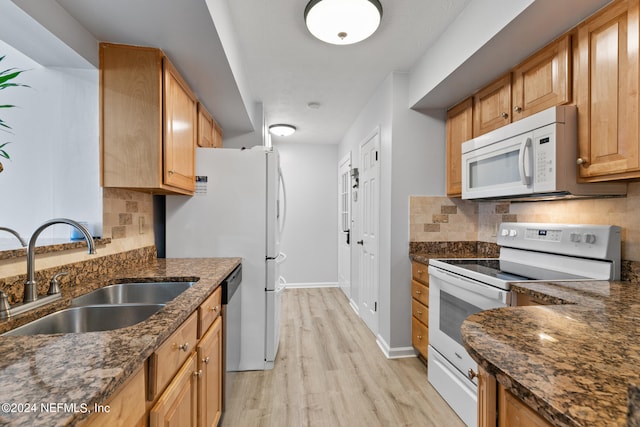 kitchen with dark stone counters, light hardwood / wood-style floors, sink, and white appliances