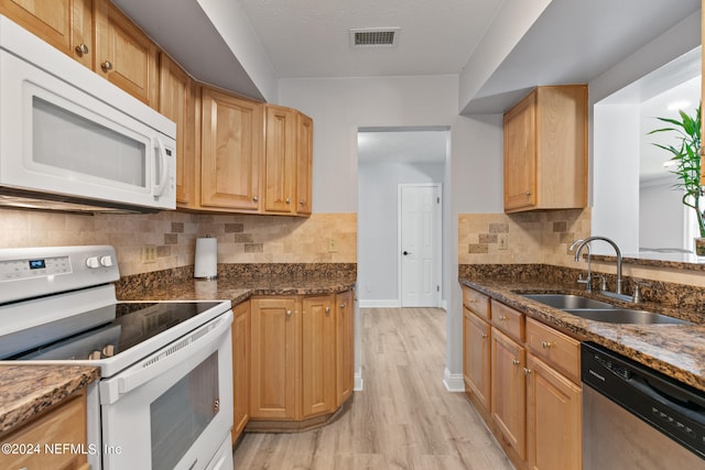 kitchen with light wood-type flooring, sink, white appliances, backsplash, and dark stone counters