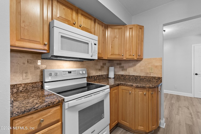 kitchen featuring dark stone countertops, light wood-type flooring, white appliances, and decorative backsplash