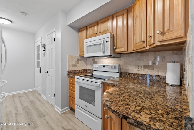 kitchen featuring dark stone countertops, light wood-type flooring, tasteful backsplash, and white appliances