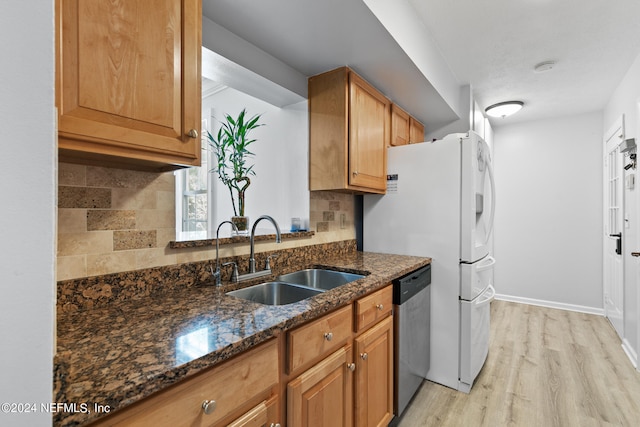 kitchen with sink, tasteful backsplash, light hardwood / wood-style flooring, appliances with stainless steel finishes, and dark stone countertops