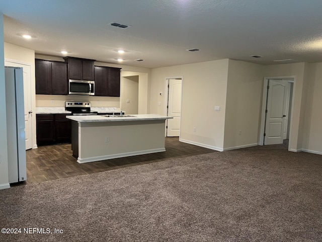 kitchen with dark brown cabinets, a textured ceiling, a center island with sink, dark wood-type flooring, and appliances with stainless steel finishes