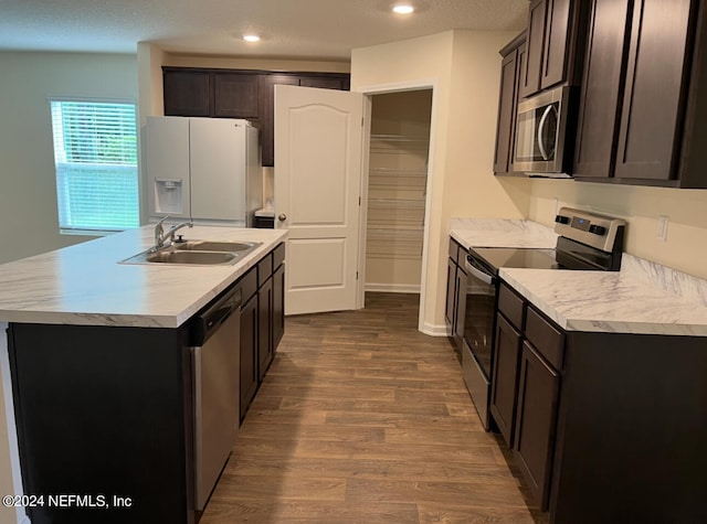 kitchen featuring an island with sink, sink, dark brown cabinets, hardwood / wood-style flooring, and appliances with stainless steel finishes