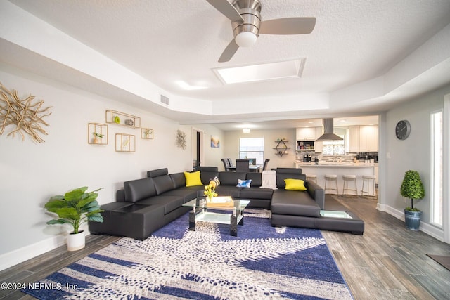 living room with a textured ceiling, a tray ceiling, dark hardwood / wood-style floors, and ceiling fan