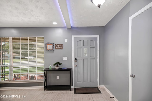 foyer with light hardwood / wood-style flooring, beam ceiling, and a textured ceiling