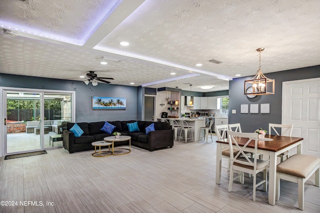 living room with a textured ceiling, ceiling fan with notable chandelier, and light hardwood / wood-style floors