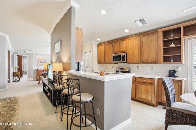 kitchen with ornamental molding, light tile patterned floors, kitchen peninsula, appliances with stainless steel finishes, and a kitchen bar