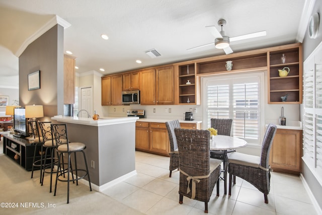 kitchen with appliances with stainless steel finishes, crown molding, kitchen peninsula, and light tile patterned floors