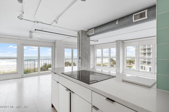 kitchen with black electric stovetop, a healthy amount of sunlight, a water view, and white cabinetry