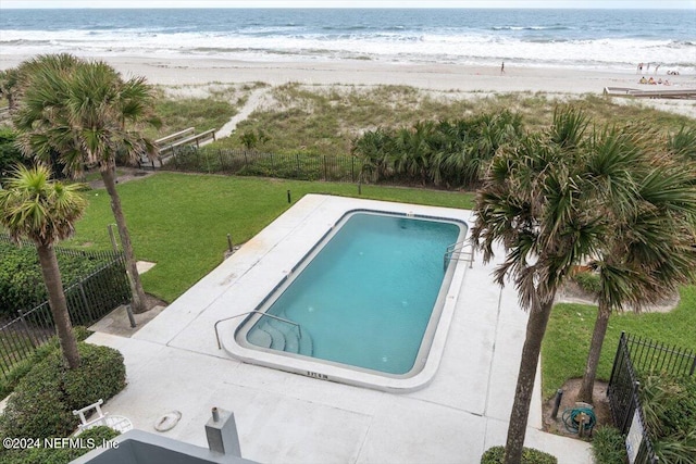 view of swimming pool featuring a lawn, a water view, a patio, and a view of the beach