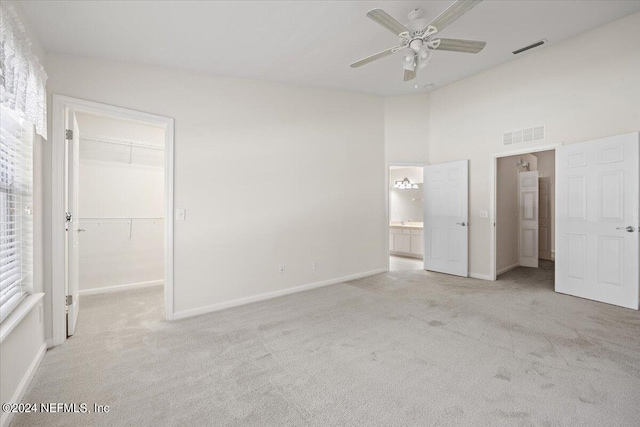 unfurnished bedroom with a spacious closet, a closet, ceiling fan, ensuite bath, and light carpet