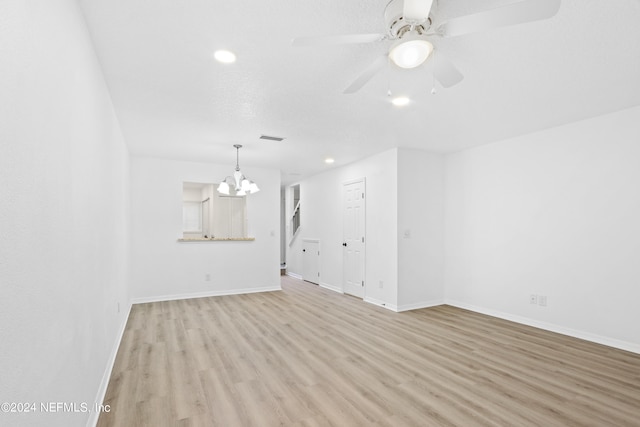 spare room with a textured ceiling, ceiling fan with notable chandelier, visible vents, baseboards, and light wood finished floors