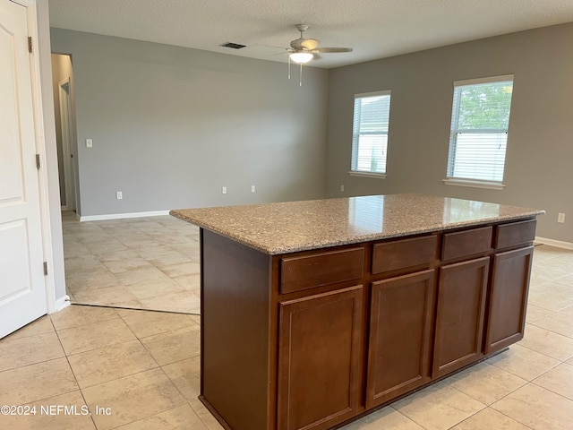 kitchen featuring light stone countertops, a textured ceiling, ceiling fan, light tile patterned floors, and a center island