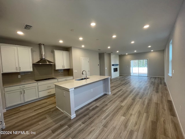 kitchen featuring black electric cooktop, sink, wall chimney exhaust hood, wood-type flooring, and white cabinets