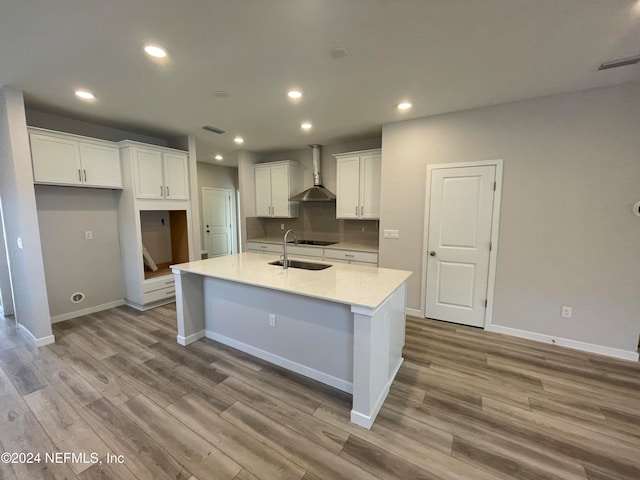 kitchen featuring white cabinetry, light stone counters, wall chimney exhaust hood, an island with sink, and light wood-type flooring