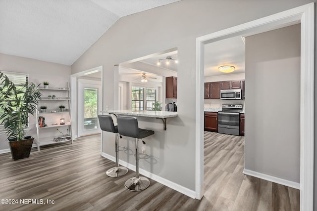 kitchen featuring light stone counters, lofted ceiling, stainless steel appliances, dark hardwood / wood-style floors, and a kitchen bar