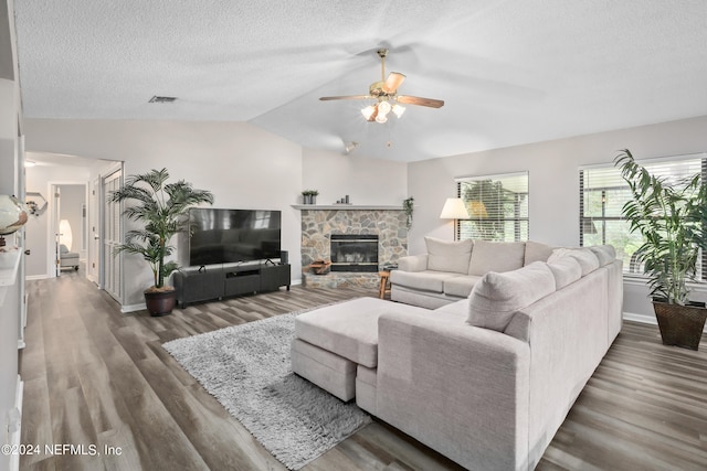 living room featuring a textured ceiling, dark hardwood / wood-style floors, vaulted ceiling, a fireplace, and ceiling fan