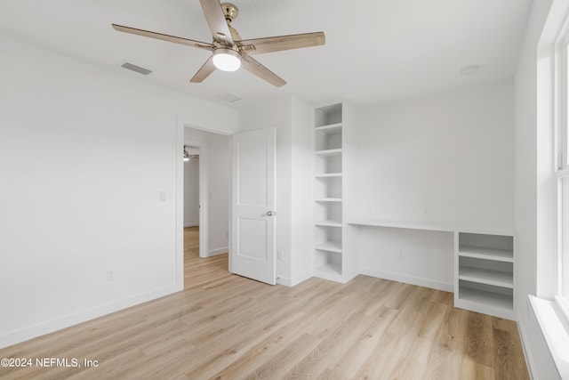 unfurnished bedroom featuring light wood-type flooring, built in desk, and ceiling fan