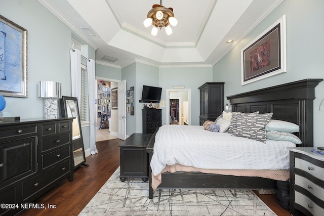 bedroom with dark wood-type flooring, a raised ceiling, a closet, crown molding, and a walk in closet