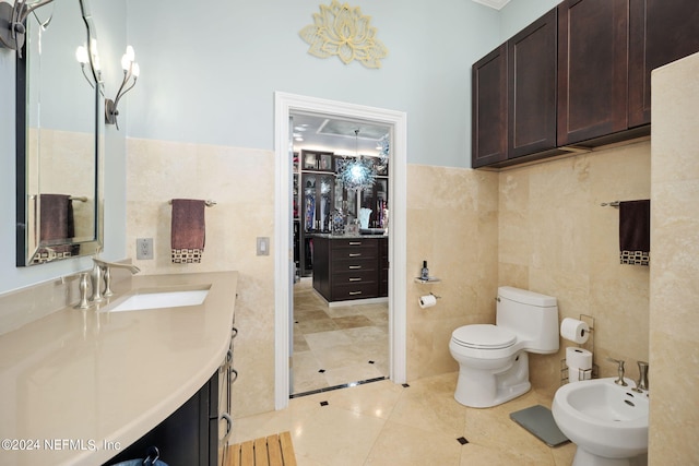 bathroom with vanity, toilet, a bidet, tile walls, and tile patterned flooring