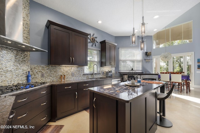 kitchen featuring stainless steel gas stovetop, a healthy amount of sunlight, sink, and wall chimney range hood