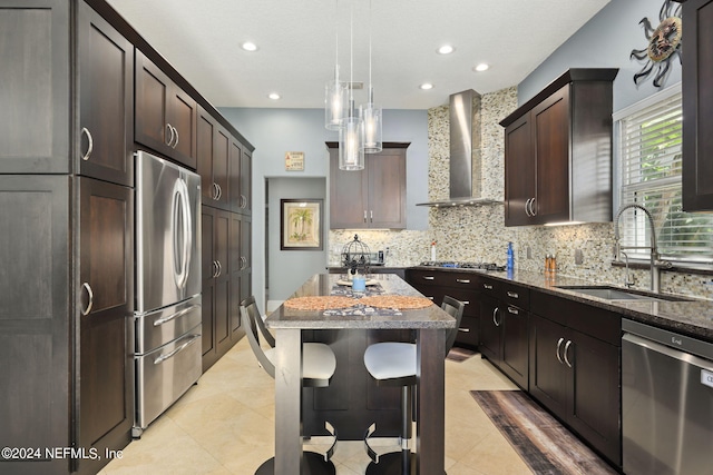 kitchen featuring dark stone counters, sink, a kitchen island, wall chimney range hood, and appliances with stainless steel finishes