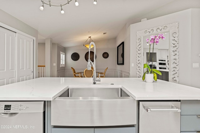 kitchen featuring vaulted ceiling, a sink, light stone counters, and white dishwasher