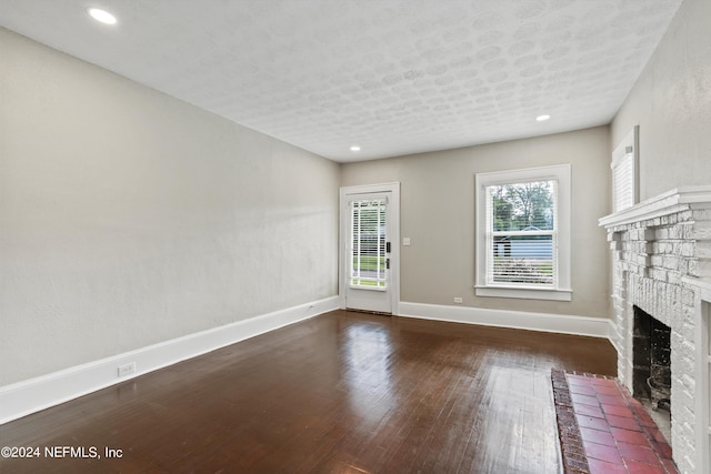 unfurnished living room featuring dark hardwood / wood-style floors, a textured ceiling, and a brick fireplace