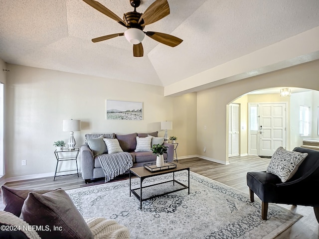 living room with a textured ceiling, ceiling fan, light hardwood / wood-style flooring, and vaulted ceiling