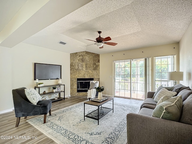 living room featuring a tile fireplace, ceiling fan, a textured ceiling, and hardwood / wood-style flooring