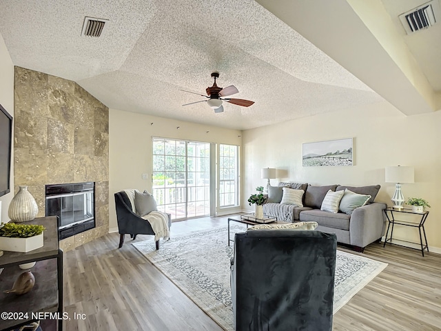 living room featuring hardwood / wood-style floors, lofted ceiling, ceiling fan, a fireplace, and a textured ceiling