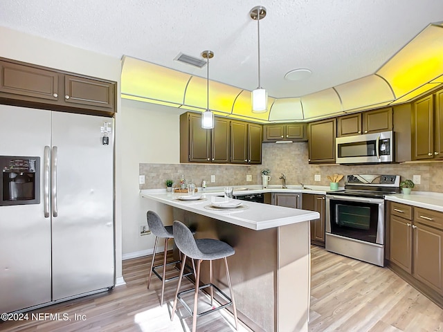 kitchen featuring a kitchen bar, appliances with stainless steel finishes, light wood-type flooring, sink, and pendant lighting