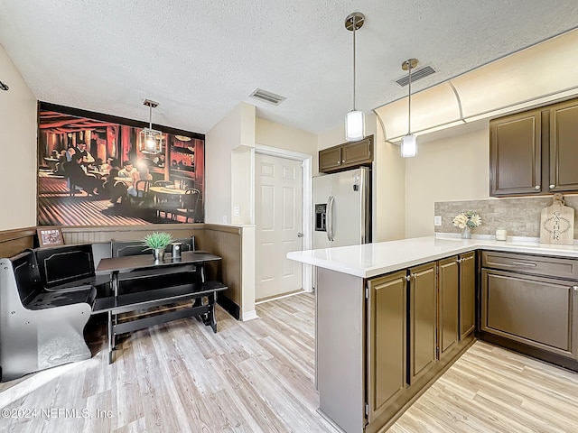 kitchen featuring kitchen peninsula, stainless steel fridge, decorative light fixtures, and light wood-type flooring