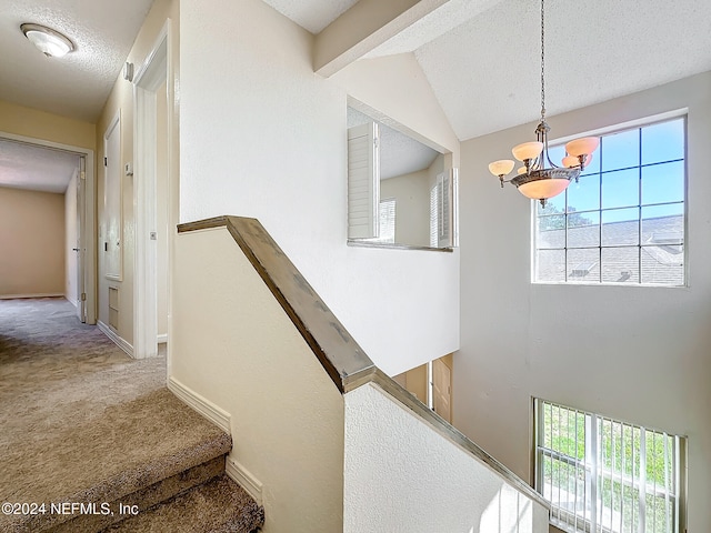 staircase with a chandelier, lofted ceiling, a textured ceiling, and carpet floors