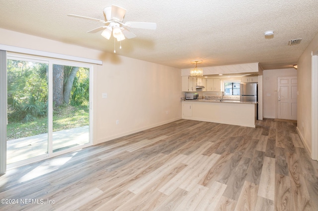 unfurnished living room with sink, light hardwood / wood-style flooring, a textured ceiling, and ceiling fan with notable chandelier